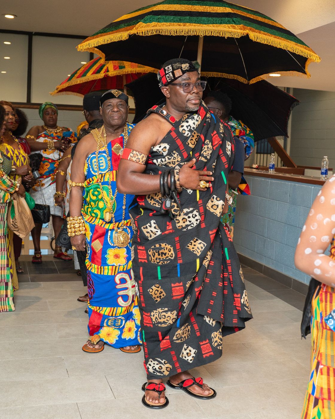 Chiefs in kente walking beneath a fringed state umbrella