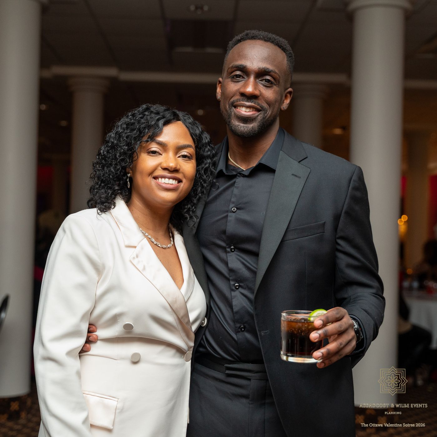 A couple smiling together, one in a white blazer