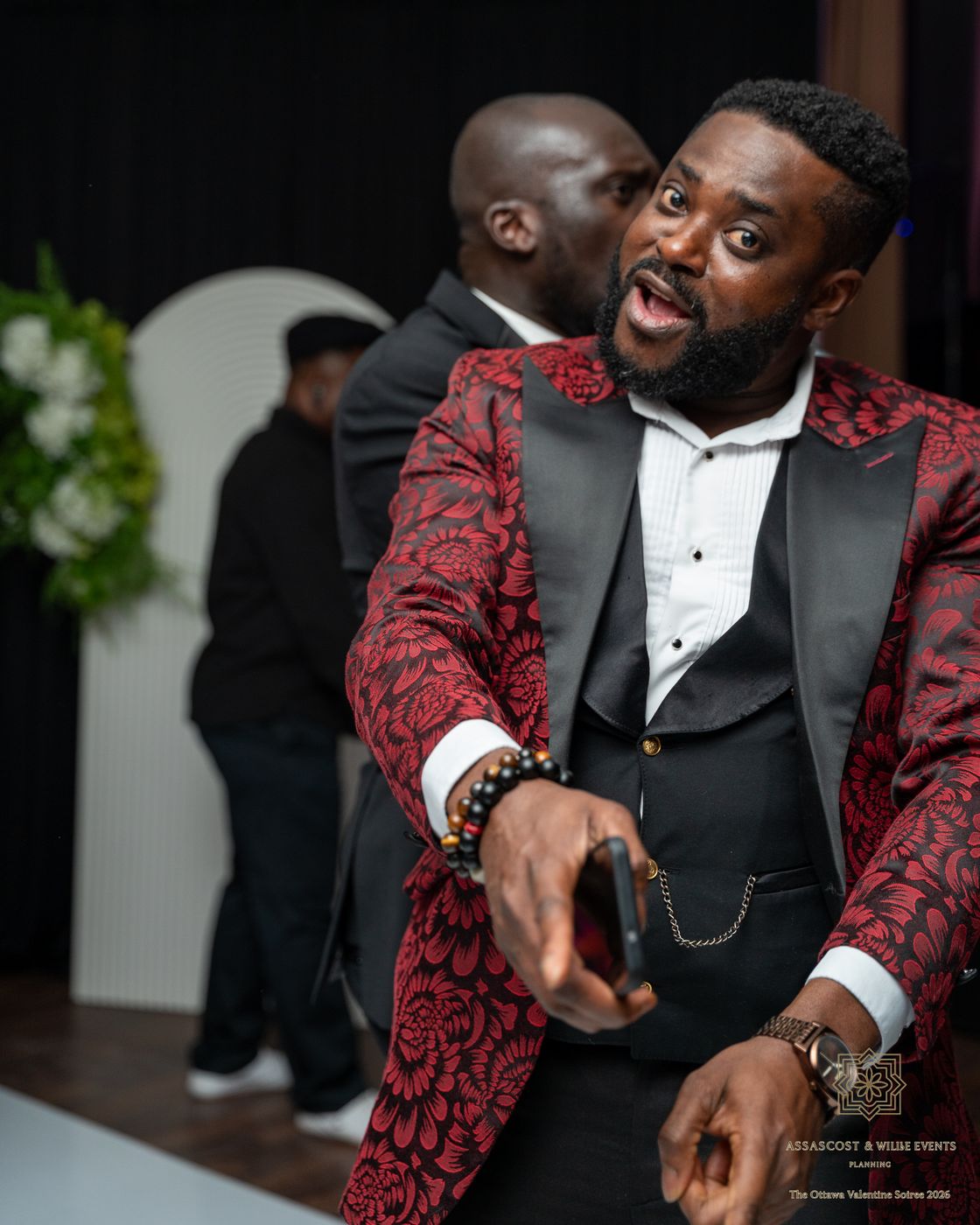 A guest in a red floral tuxedo jacket pointing at the camera