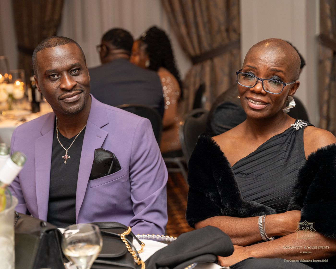 Two guests seated together, one in a lilac blazer and one in a black dress with a fur wrap